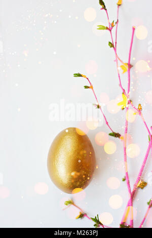 Golden egg on white background with pink branches with buds, easter background with copy space Stock Photo
