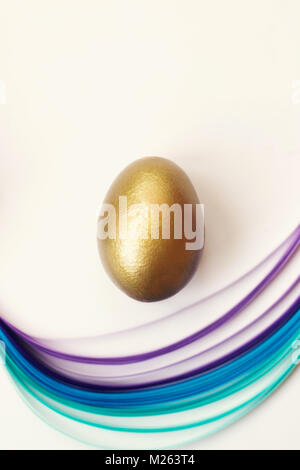 Golden egg on white background, decorated with blue and violet paper stripes Stock Photo
