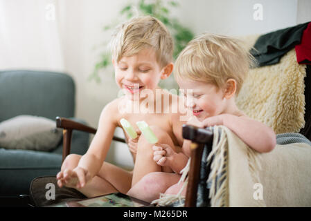 Two brothers eating ice cream in the recliner while enjoying Internet movie clips on the tablet. Stock Photo