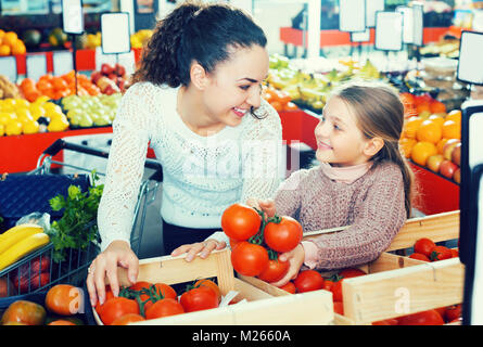 Happy young woman and small girl buying red tomatoes in supermarket Stock Photo
