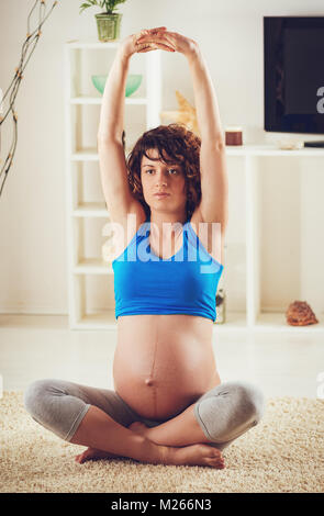 Beautiful young pregnant woman doing yoga exercise at the home. Stock Photo
