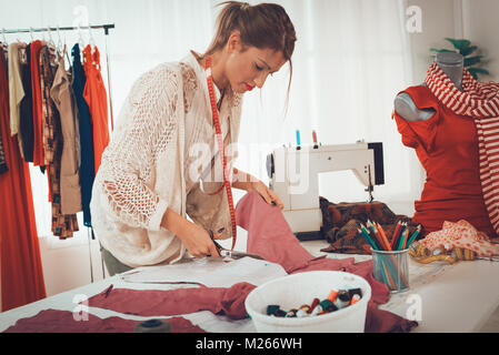 Beautiful young woman with tape measure over the neck, cut with scissors material by sewing pattern. Stock Photo