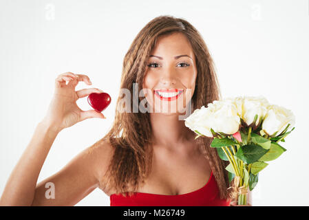 Portrait of a beautiful smiling girl holding a red heart and bouquet of white roses. Looking at camera. Stock Photo