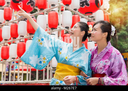 beautiful young female travelers standing in front of celebration lantern decorations and pointing local landscape when they travel in japan with trad Stock Photo