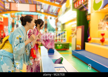 cheerful young woman wearing traditional kimono clothing together and playing Daruma game in market with selective focus photo. Stock Photo
