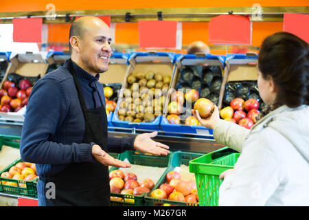 Young woman purchasing seasonal fruits in grocery from mature charming  seller Stock Photo