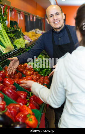 Charming elderly salesman serving female buyer purchasing veggies in supermarket Stock Photo