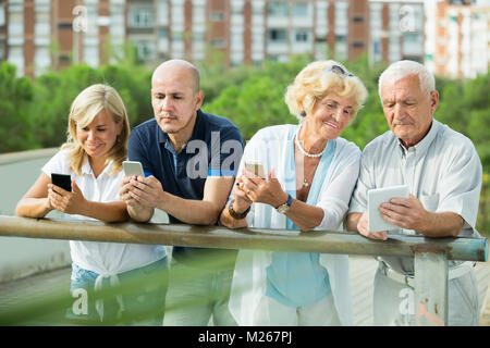 Portrait of positive mature couples using gadgets in park outdoor Stock Photo