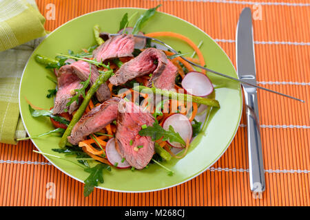 Mixed spring salad with roasted asparagus and medium fried beef steak cut into strips Stock Photo