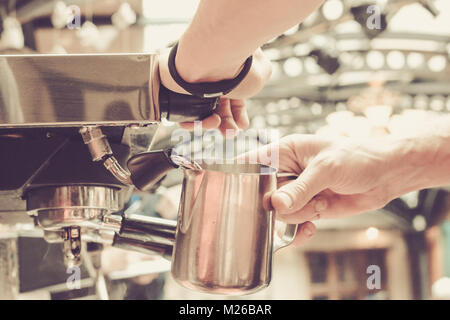 Barista is steaming milk for cappuccino or latte using professional coffee machine in the cafe, Shallow depth of field, pastel color toning Stock Photo