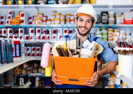 Positive  workman holding basket with picked tools in paint store Stock Photo