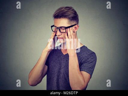 Young casual man in eyeglasses rubbing temples with eyes closed trying to remember information. Stock Photo