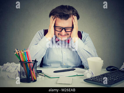 Chunky man in eyeglasses rubbing temples looking burnout while working at table in mess. Stock Photo