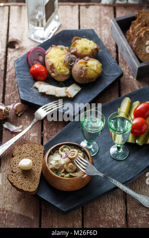Pickled tomatoes, cucumbers, mushrooms and onion on wooden background with fork and shots of vodka Stock Photo
