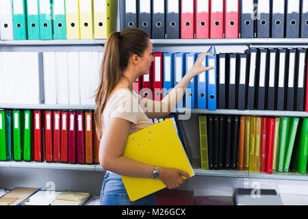 Woman is choosing folders on the shelves in stationery store. Stock Photo