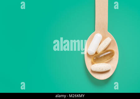 Wooden teaspoon with healthy vitamins and minerals against pastel green background Stock Photo