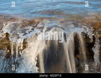 Small waterfall covered in ice but the water is still flowing down Stock Photo