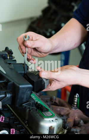 A young male apprentice works on a car engine while training to be a mechanic. Stock Photo