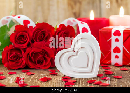 Shape of white heart in front of bouquet of red roses and candles on wooden background. Valentines day concept. Motherâ€™s day concept! Focus on heart Stock Photo