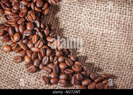 Roasted coffee beans lying on coarse jute cloth in top view in hard sidelight. Stock Photo