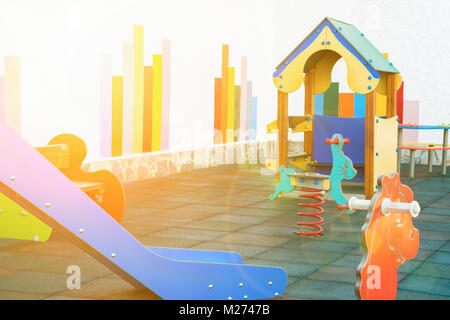 Small Empty Children Playground of a Kindergarten in a European City. Colorful Wooden House Seesaw Slide Soft Rubber Ground. Outdoors Summer Golden Su Stock Photo