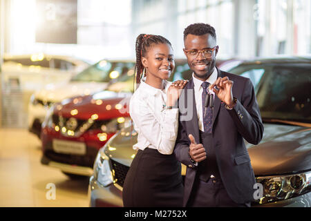 Visiting car dealership. couple holding key of their new car, looking at camera Stock Photo