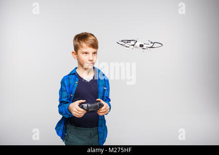 Cute boy operating the dron or quadcopter by remote control on grey background. Stock Photo