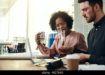 Two designers using a laptop and discussing color swatches while sitting together at a table in a modern office Stock Photo