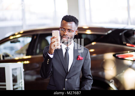 african car salesman using smart phone in showroom Stock Photo