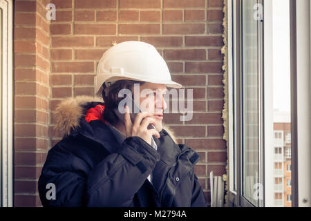 Young civil engineer is having trouble over the phone against brick background. Soft focus, toned. Stock Photo