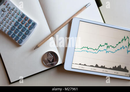 Close up view an ethereum silver, a stock graph on a tablet screen and blank note with calculator Stock Photo
