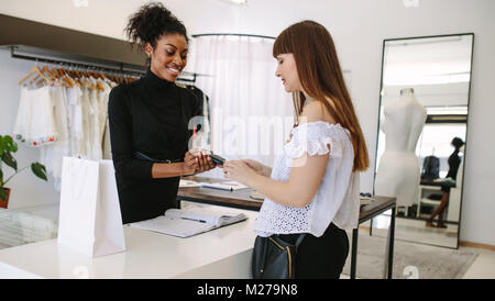 Customer shopping designer wear at a fashion boutique. Customer making payment using a credit card on a point of sale machine. Stock Photo
