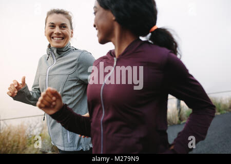 Two happy women going for sunrise running. Women in track suits running on road. Stock Photo