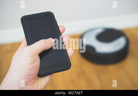 Man using mobile to control robotic vacuum cleaner. Stock Photo