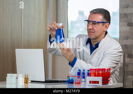 Glass laboratory chemical test tubes with red and blue liquid on white table. Stock Photo