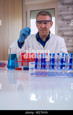 Scientist adding solution to test tubes in laboratory. Glass laboratory chemical test tubes with red and blue liquid.Man wears protective goggles and  Stock Photo