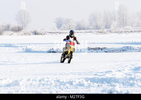 closeup man biker rides a motorcycle on a snowy hill during Cup of winter motocross. Extreme biker rides through the snow in winter, off-road bike. Wi Stock Photo