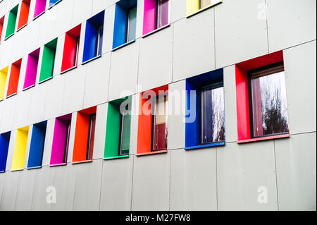 Facade of a recently renovated building with exterior insulation, covered with grey metallic panels and which window frames are painted with vivid col Stock Photo