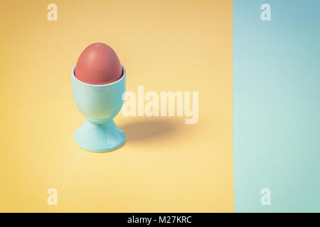 Pastel colour composition with boiled egg in cup on plain yellow and blue background Stock Photo