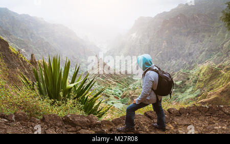 Traveler with backpack looking over the rural landscape with mountain peaks and ravine in dust air on the path from Xo-Xo Valley. Santo Antao Island, Cape Verde Stock Photo