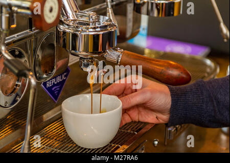 Coffee pouring into cup made by a professional barista using a coffee machine . Stock Photo