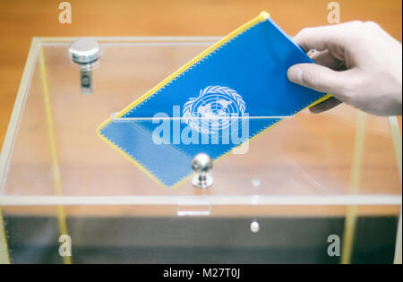 Man inserting Flag of United Nations into ballot box, voting and elections in United Nations. Stock Photo