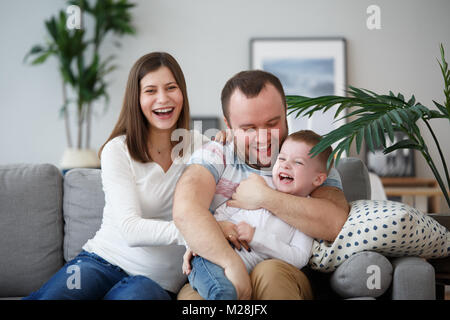 Family image of happy parents with son sitting on gray sofa Stock Photo