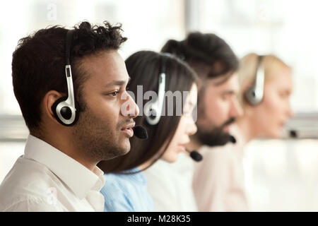 Black call center operator with colleagues. Side view of line of call centre employees are smiling and working on computers. Stock Photo
