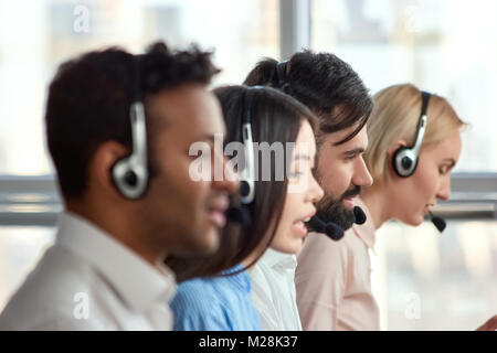 Bearded caucasian man working in call center amoung colleagues. Young bearded male employee working with a headset and accompanied by his team. Stock Photo