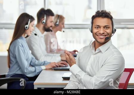 Call center operator pointing at his colleagues. Indian handsome young man pointing at his coworkers. They are working. Stock Photo