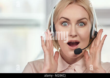 Portrait of extremely surprised woman with headset. Excited woman with headset opens mouth widely being shocked and glad, rejoices positive news. Stock Photo