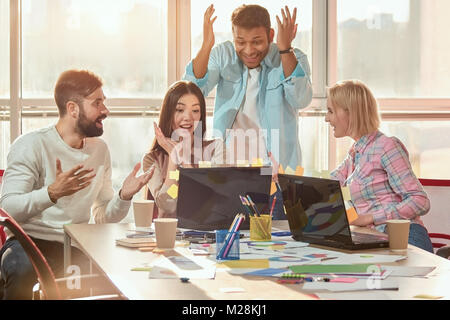 Shocked colleagues looking at laptop. Co-workers extremely wondering about content on laptop. Bright windows background. Stock Photo