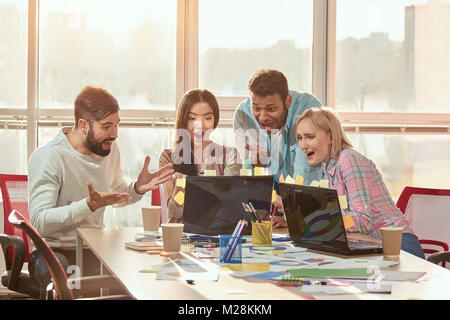 Students having fun and cooperating and working with computer. Four programmers in casual cloth working in a software developing company office. Stock Photo