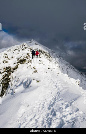 Hikers hiking up hill on south ridge at Bwlch Main to summit of Snowdon with snow in winter in Snowdonia National Park. Rhyd Ddu, Gwynedd, Wales, UK Stock Photo